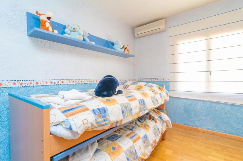 A bright bedroom with a bunk bed, patterned bedding, and a blue shelf with toys.