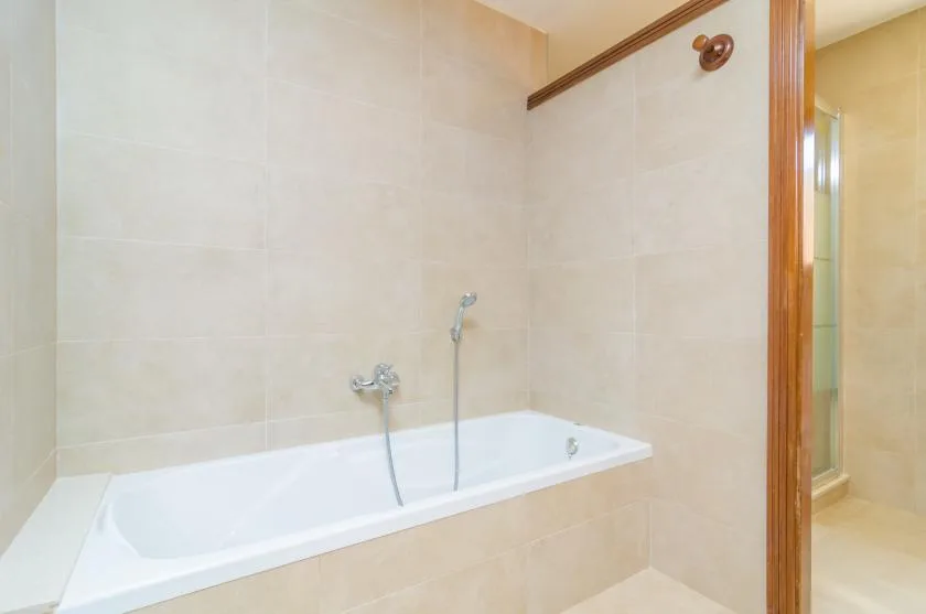 A bathroom with a white bathtub and tiled walls.