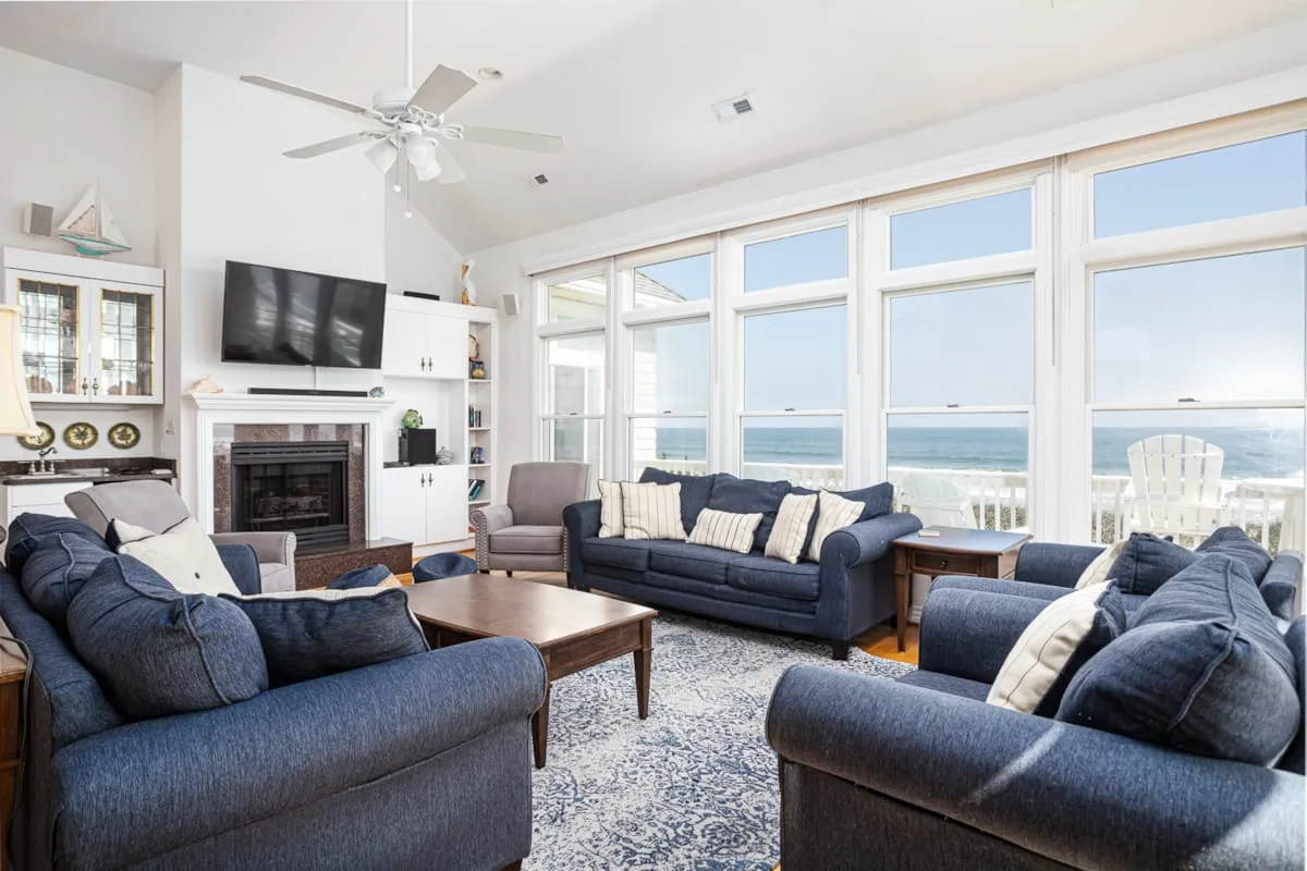 A bright living room with seating arranged around a coffee table and large ocean-facing windows.
