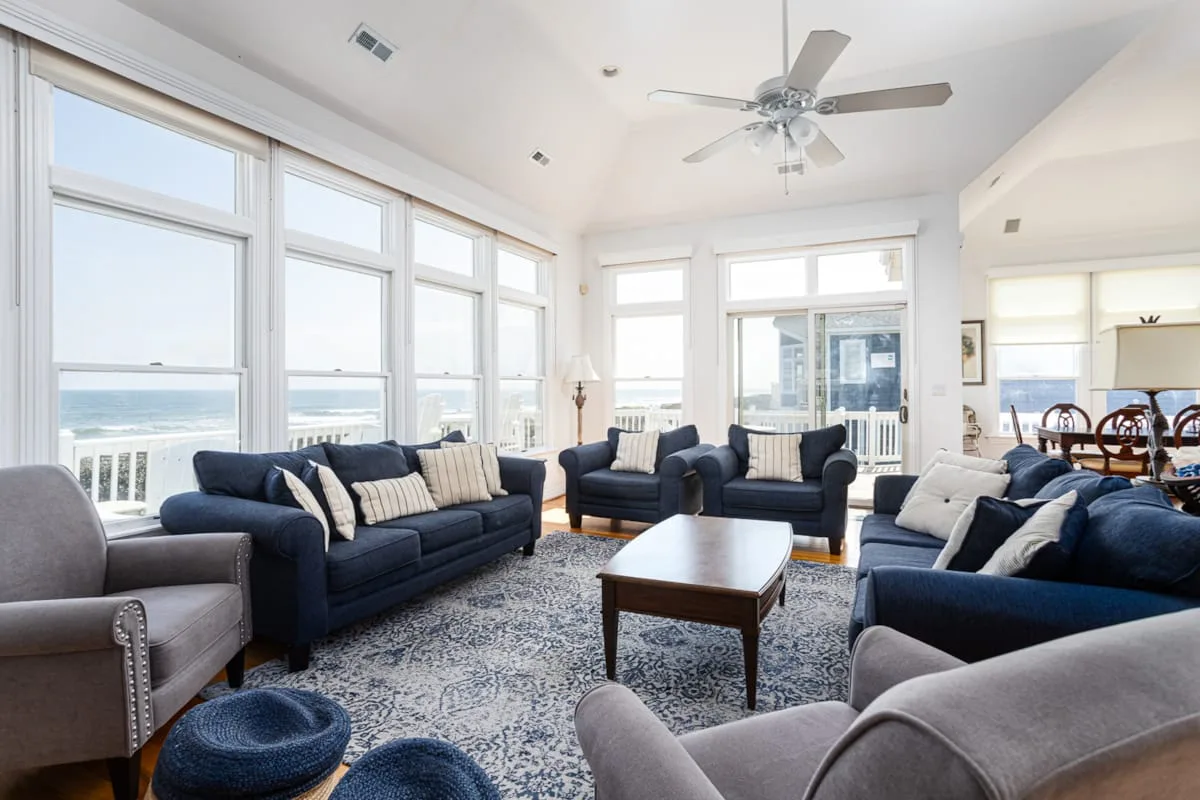 A bright living room with ample seating, a coffee table, and large windows overlooking the water.