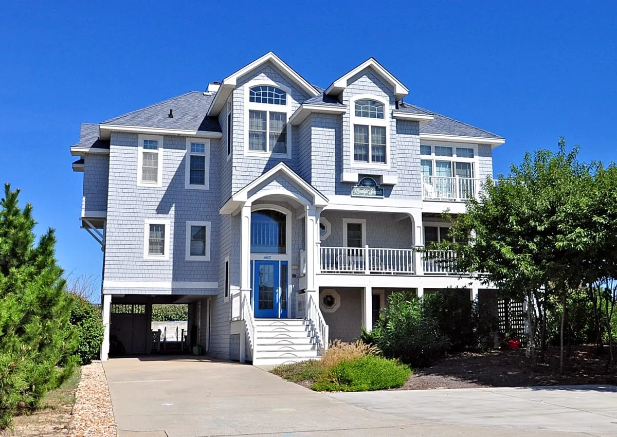 A large blue house with white trim, a driveway, and a covered porch.