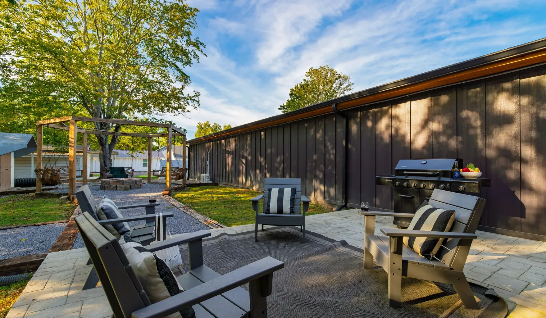 An outdoor patio with seating and a barbecue beside a dark-sided building.