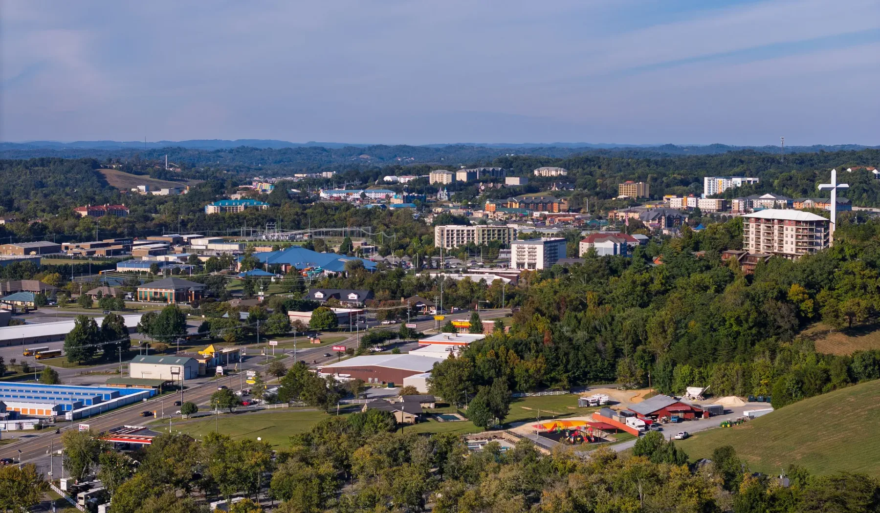 A broad view of a town with buildings, roads, and wooded hills in the distance.