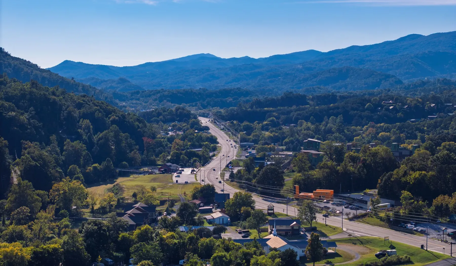 A winding road runs through a wooded valley beneath distant mountain ridges.
