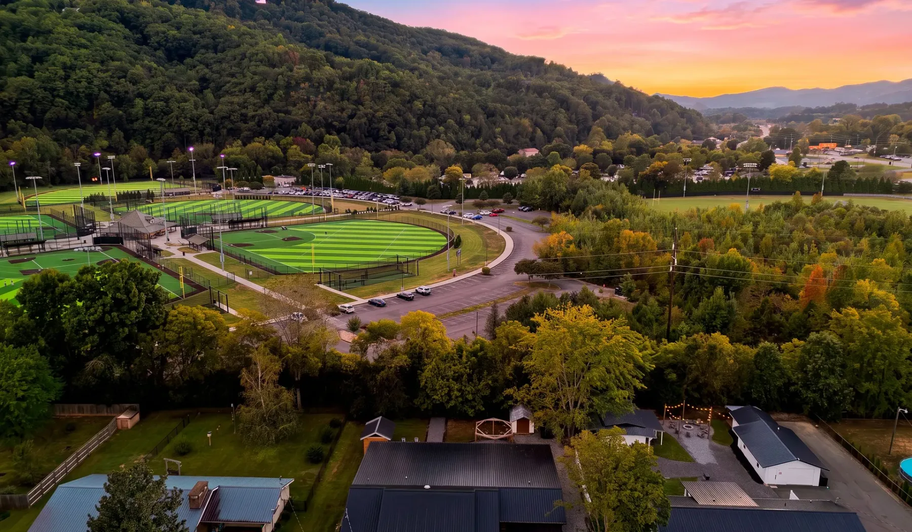 An aerial view of sports fields and homes nestled among wooded hills at sunset.