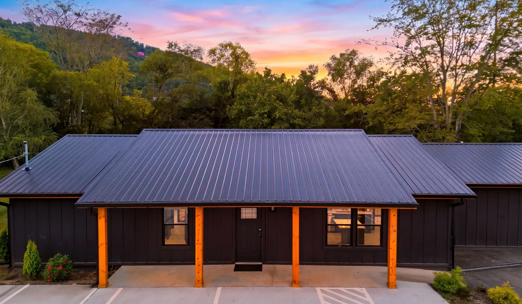 A dark building with a broad metal roof stands beneath a colorful sunset sky.