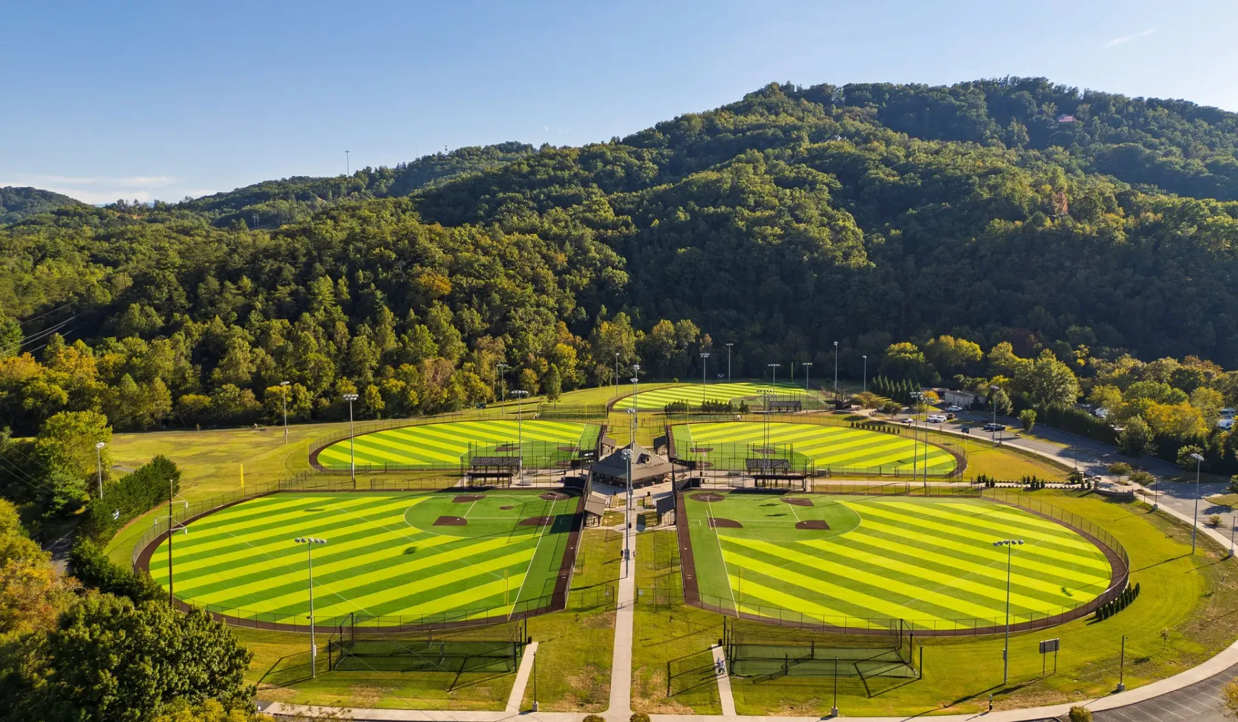 Aerial view of striped green sports fields beside wooded hills.
