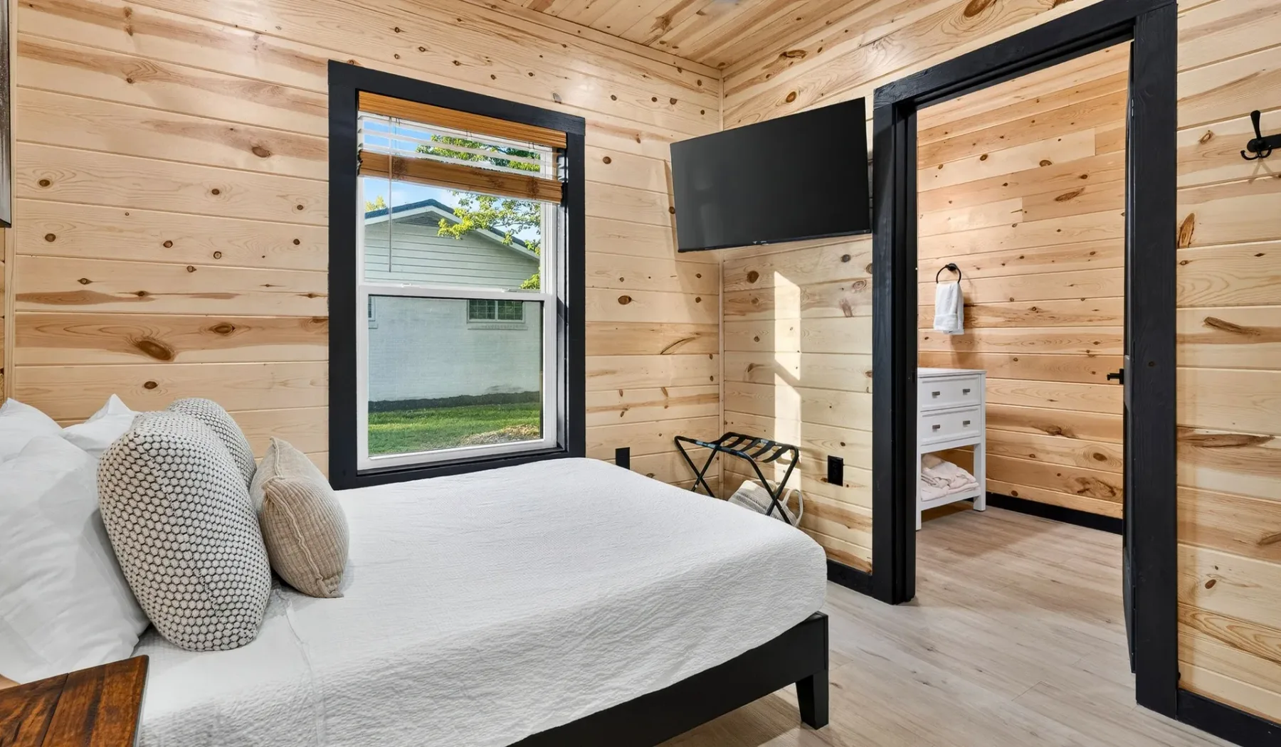 A bedroom with a white bed, a window, and a wall-mounted television.