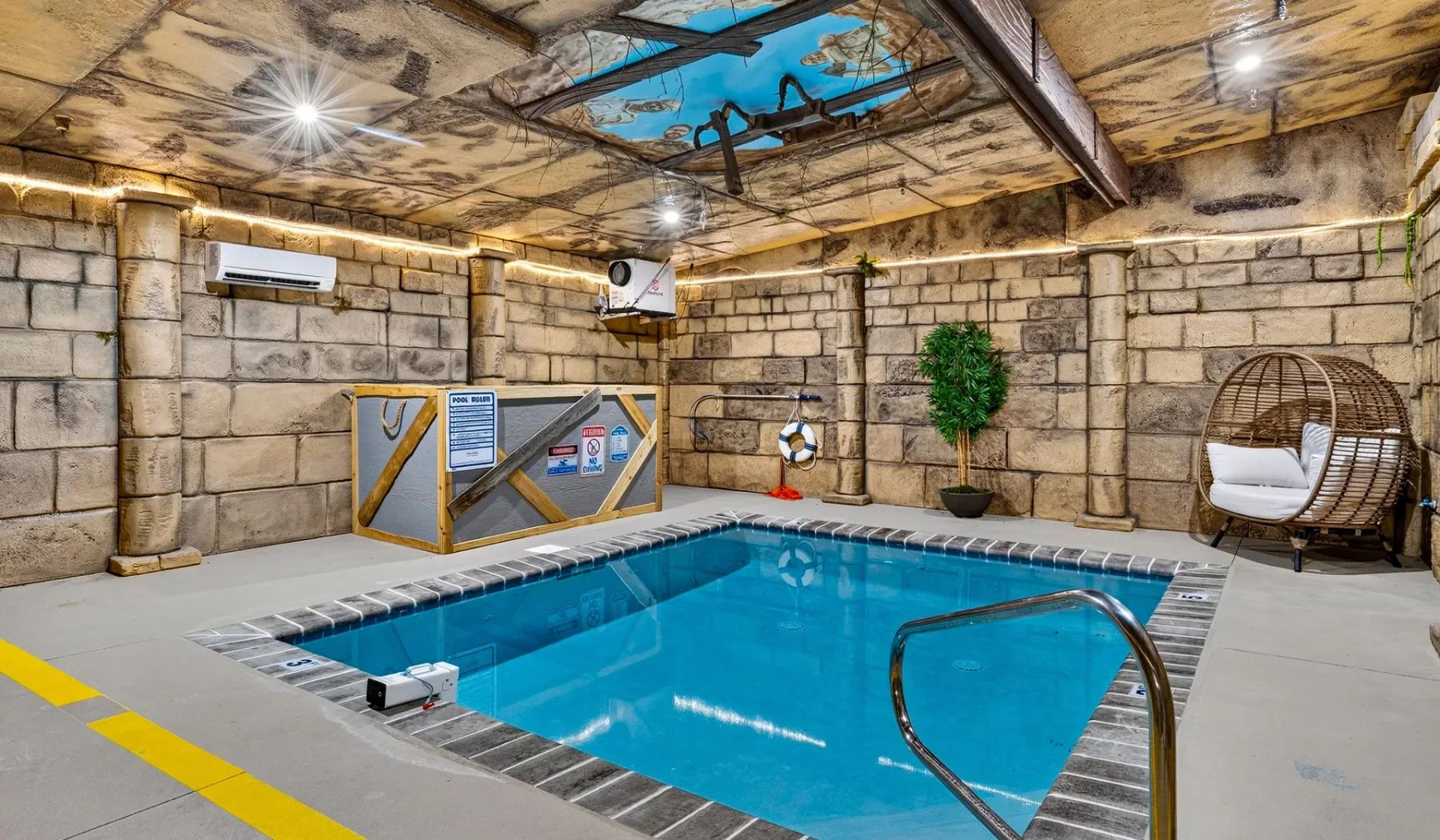 Una piscina cubierta está bajo un techo decorado, con paredes de aspecto pétreo.