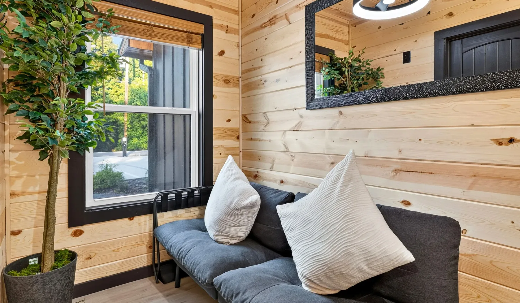 A compact seating area with a dark couch, pillows, and a large window.
