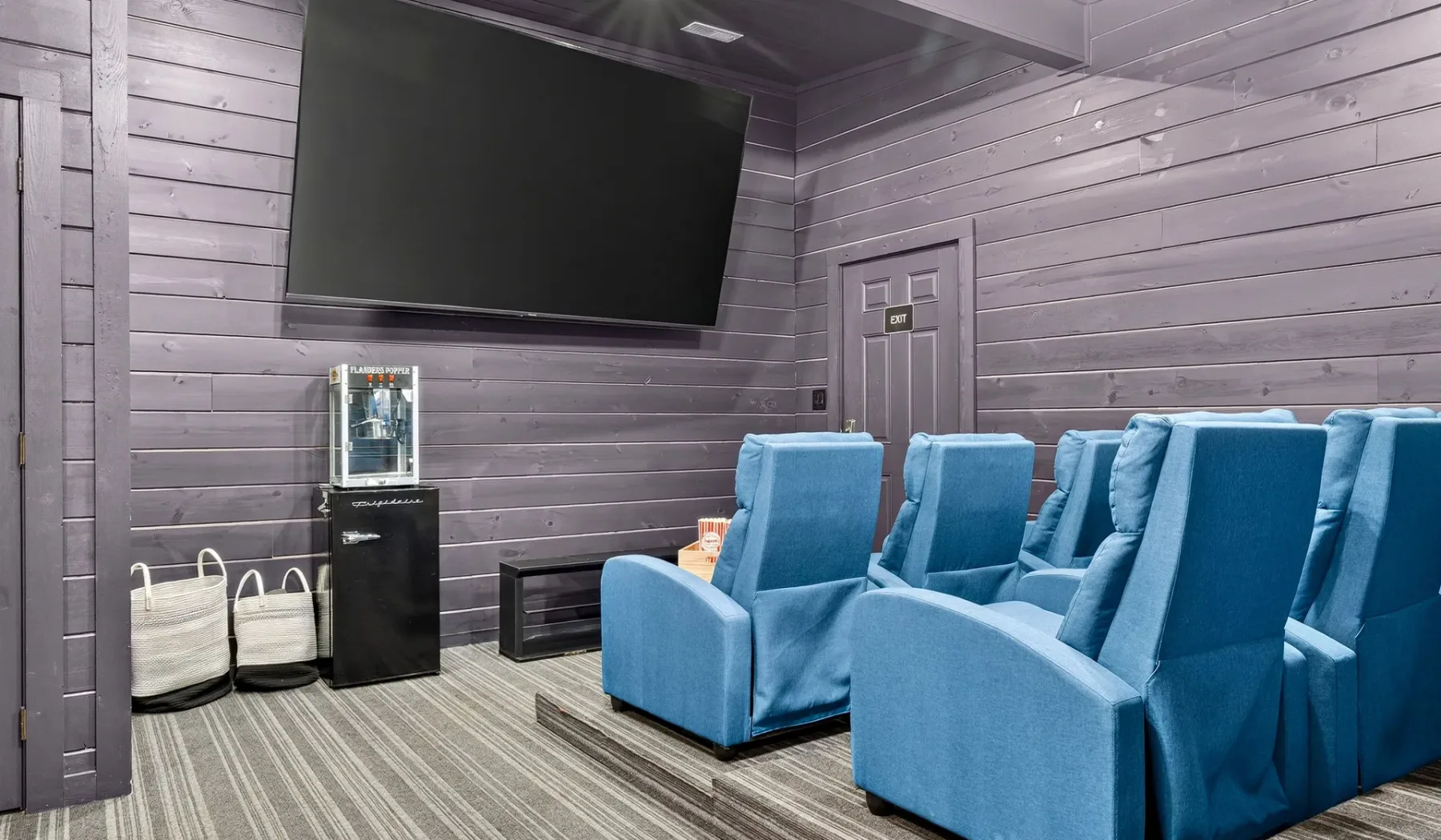 Una sala de proyección con filas de asientos azules frente a un televisor grande.