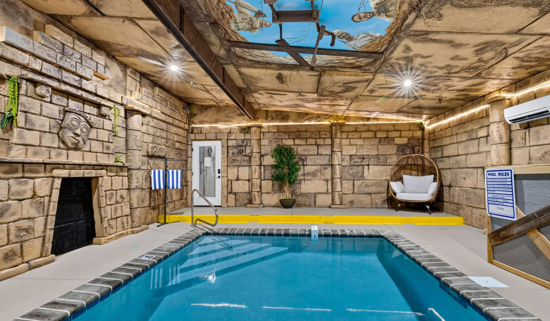 An indoor swimming pool sits beneath a decorated ceiling, with stone-patterned walls.