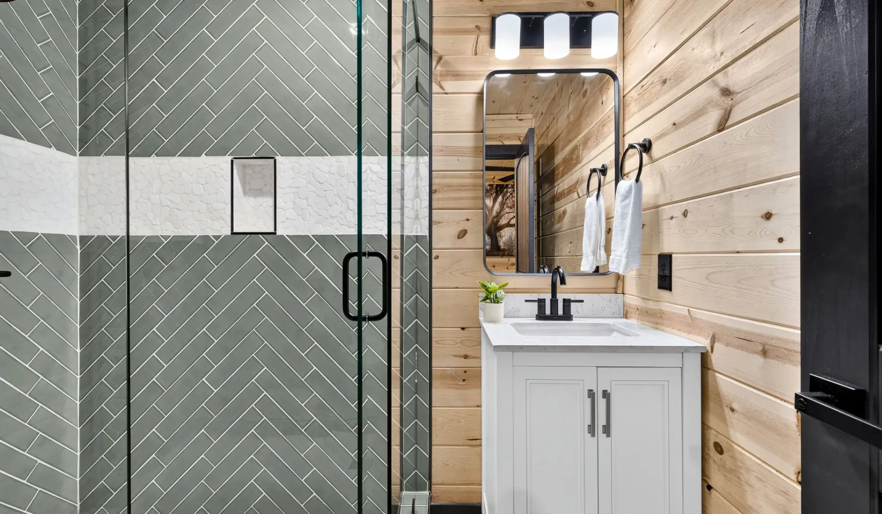 A bathroom with a glass shower beside a vanity and mirror.