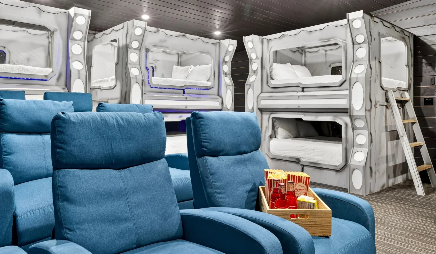 A lounge with blue seating faces a row of built-in sleeping bunks.