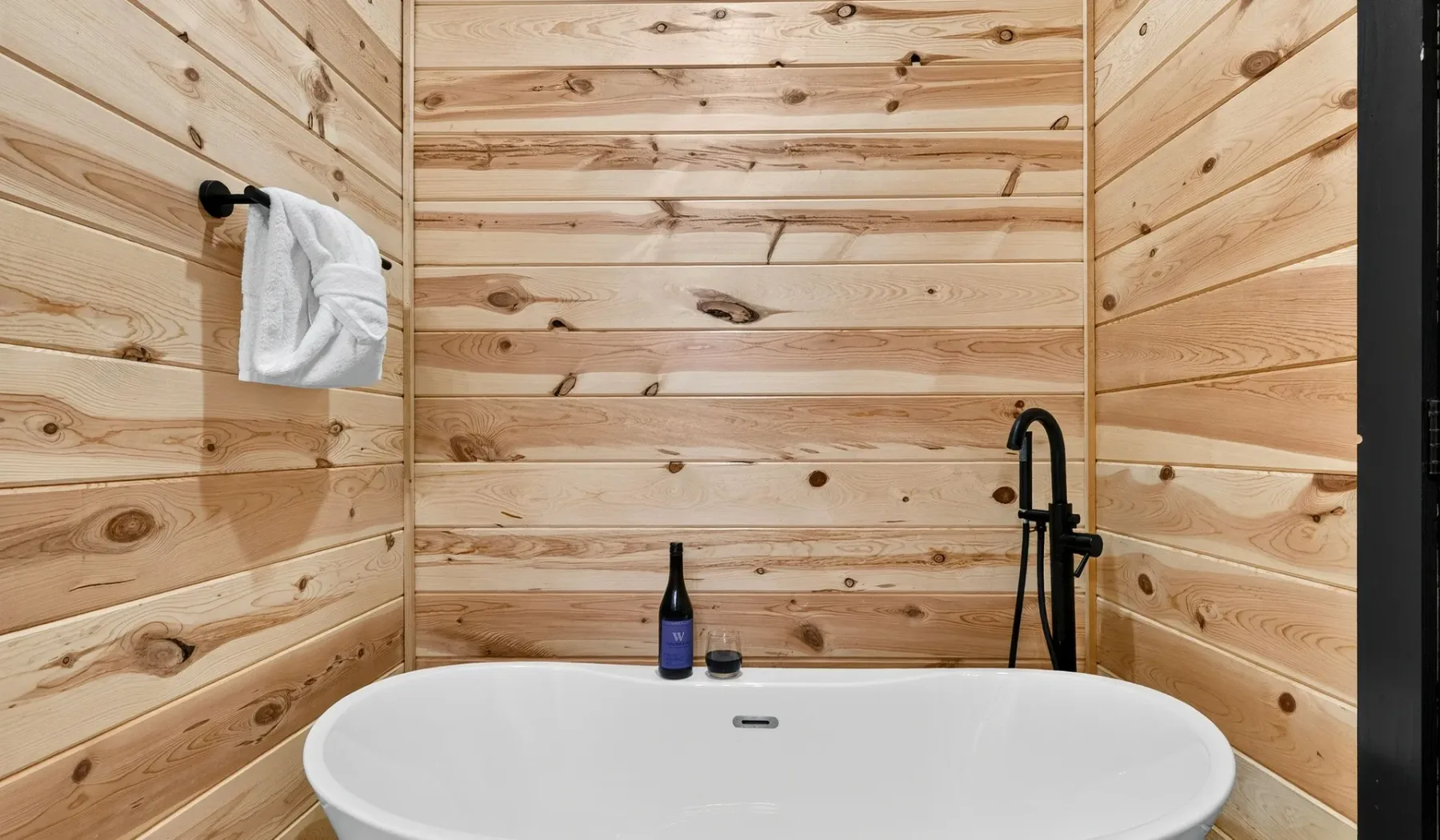 A bathtub sits in a wood-paneled bathroom with a wall-mounted shower.