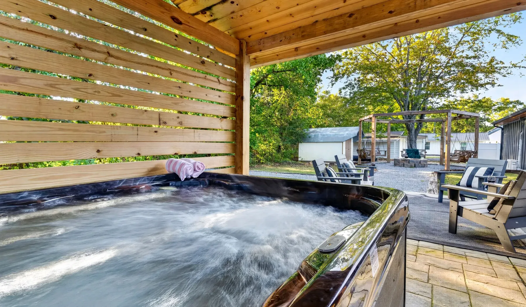 An outdoor hot tub sits beneath a wooden shelter beside a patio.