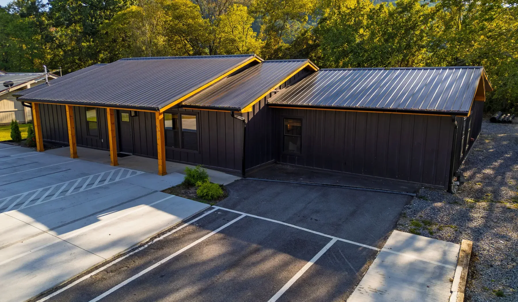 Aerial view of a dark building with metal roofs beside a marked parking area.