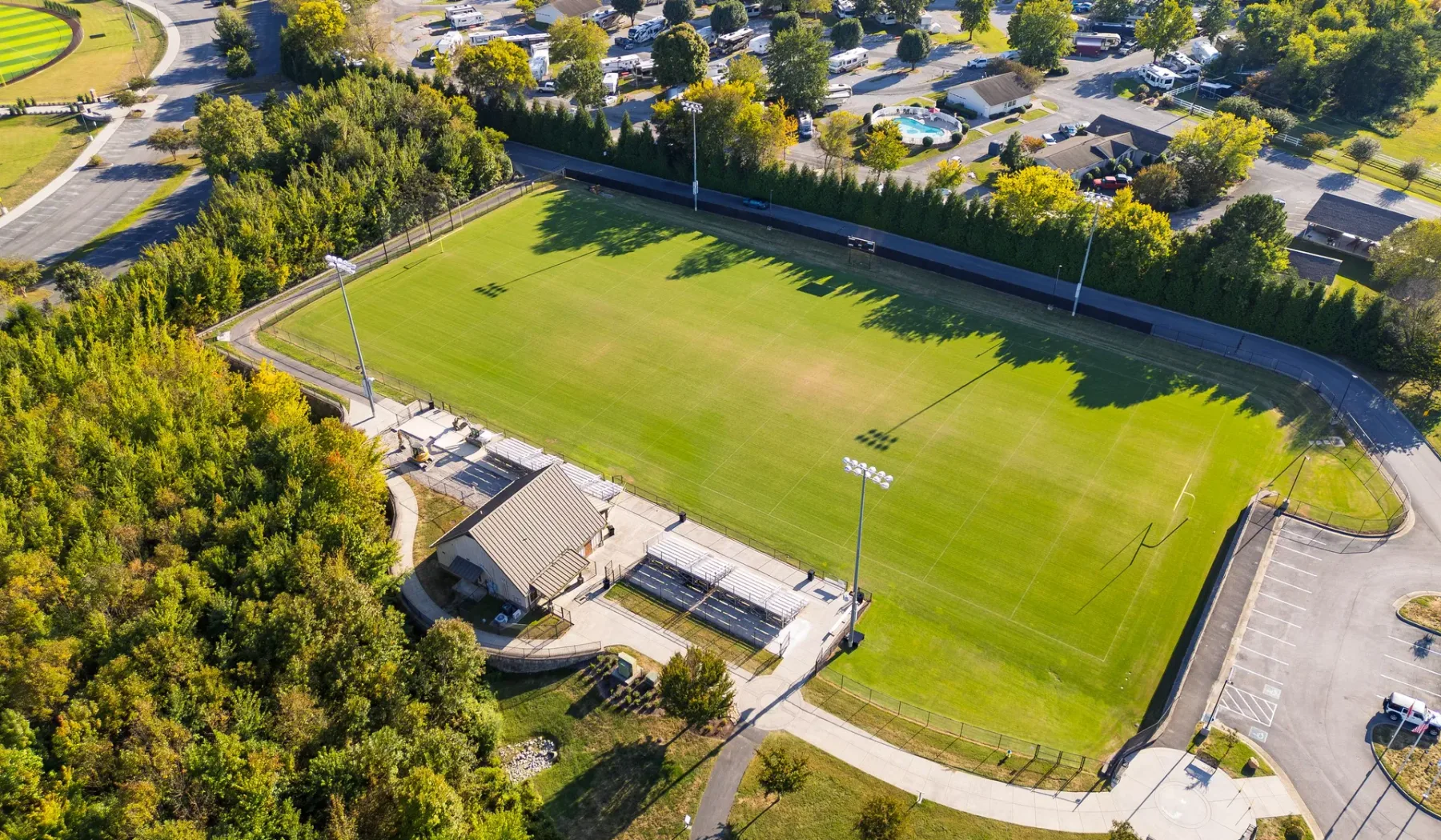 An aerial view of a green sports field surrounded by trees and paved paths.