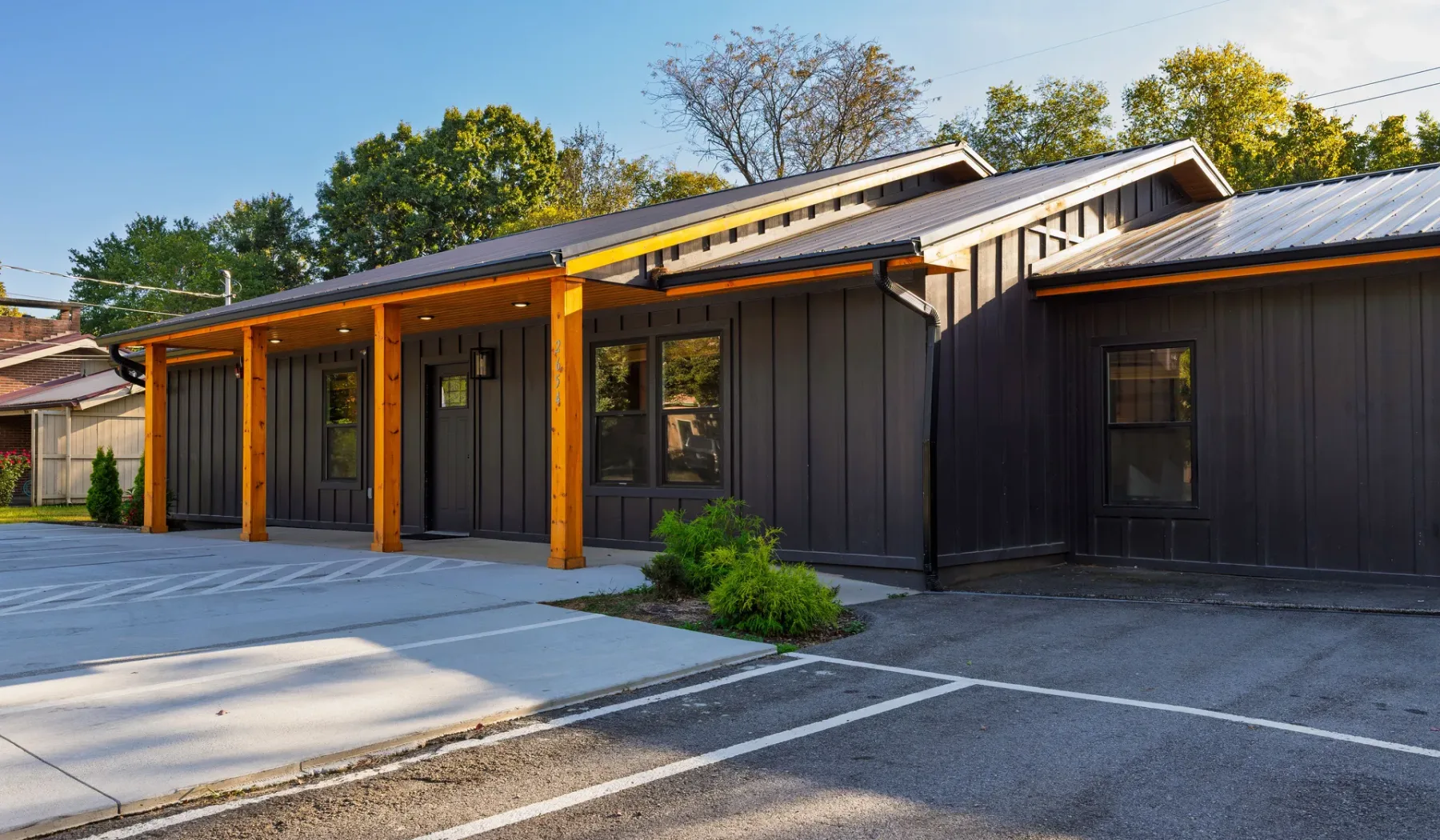 A dark-sided building with orange trim faces a paved parking area.