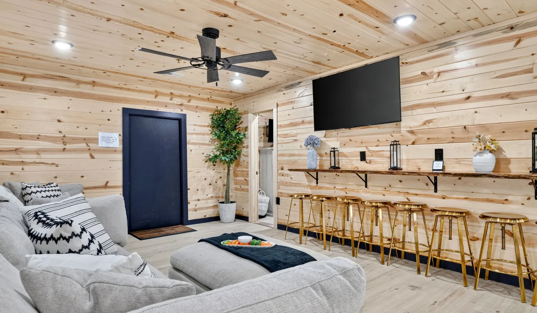A wood-paneled lounge has gray seating, a wall-mounted television, and a counter with stools.