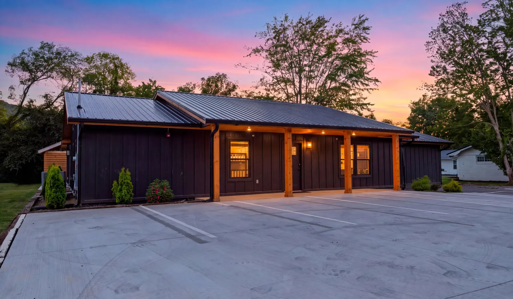 A dark-sided building faces a paved parking area beneath a colorful sunset sky.