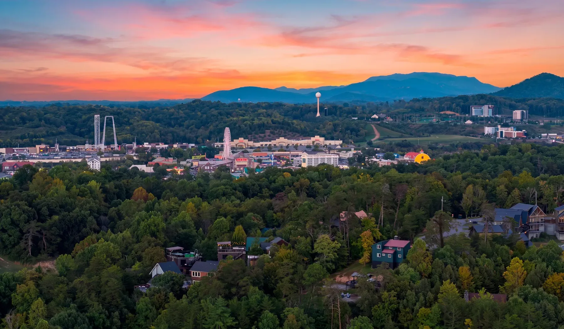 A town and wooded hills sit beneath a colorful sunset sky.