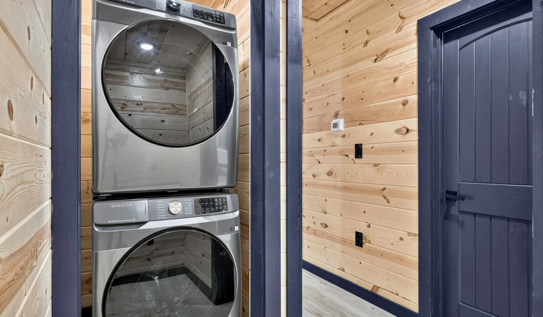 A laundry area with stacked washer and dryer beside a dark door.