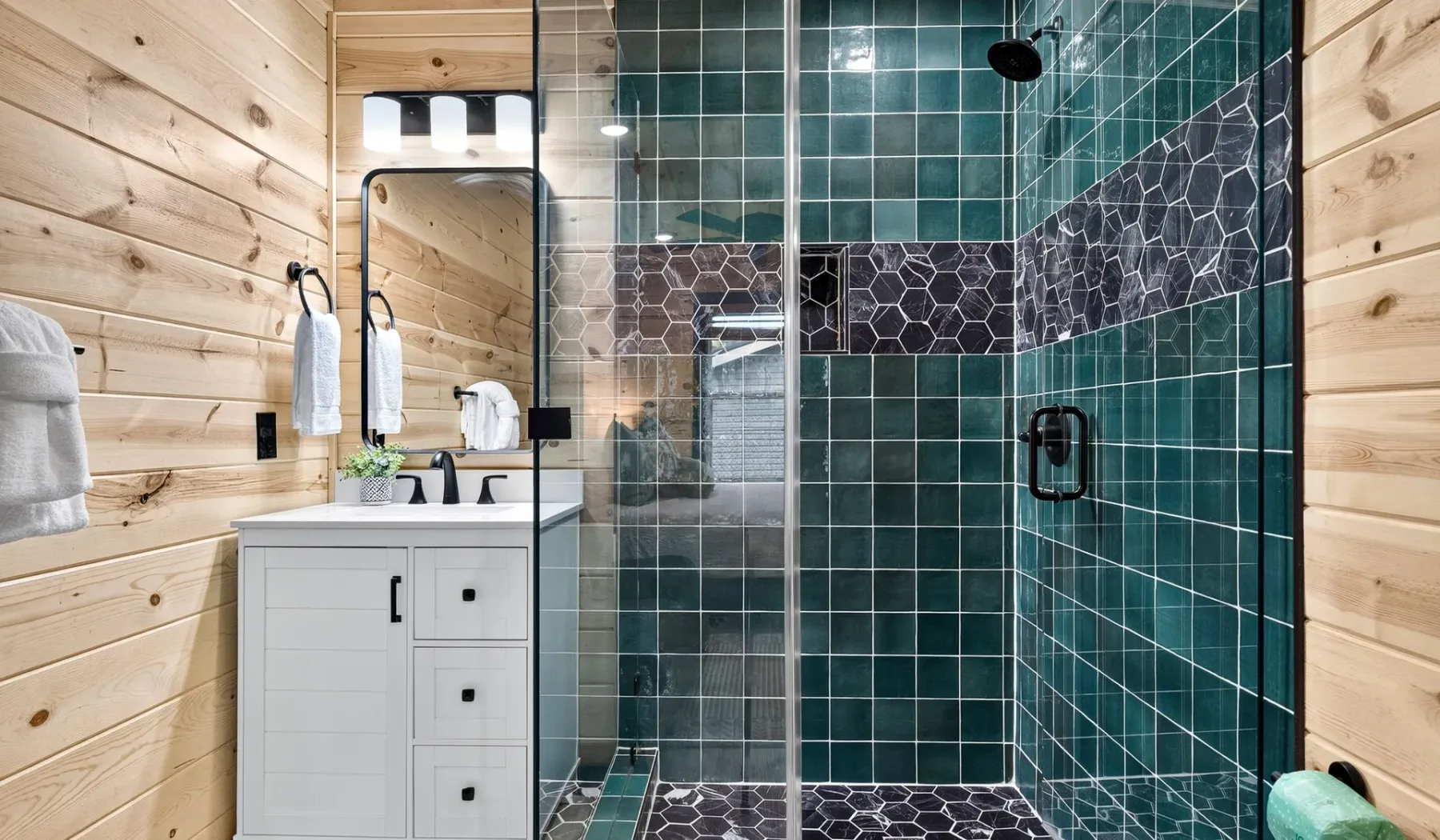 A bathroom with a tiled shower beside a white vanity and wood-paneled walls.