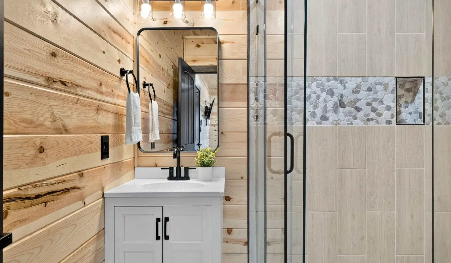 A bathroom vanity with a mirror stands beside a glass shower.