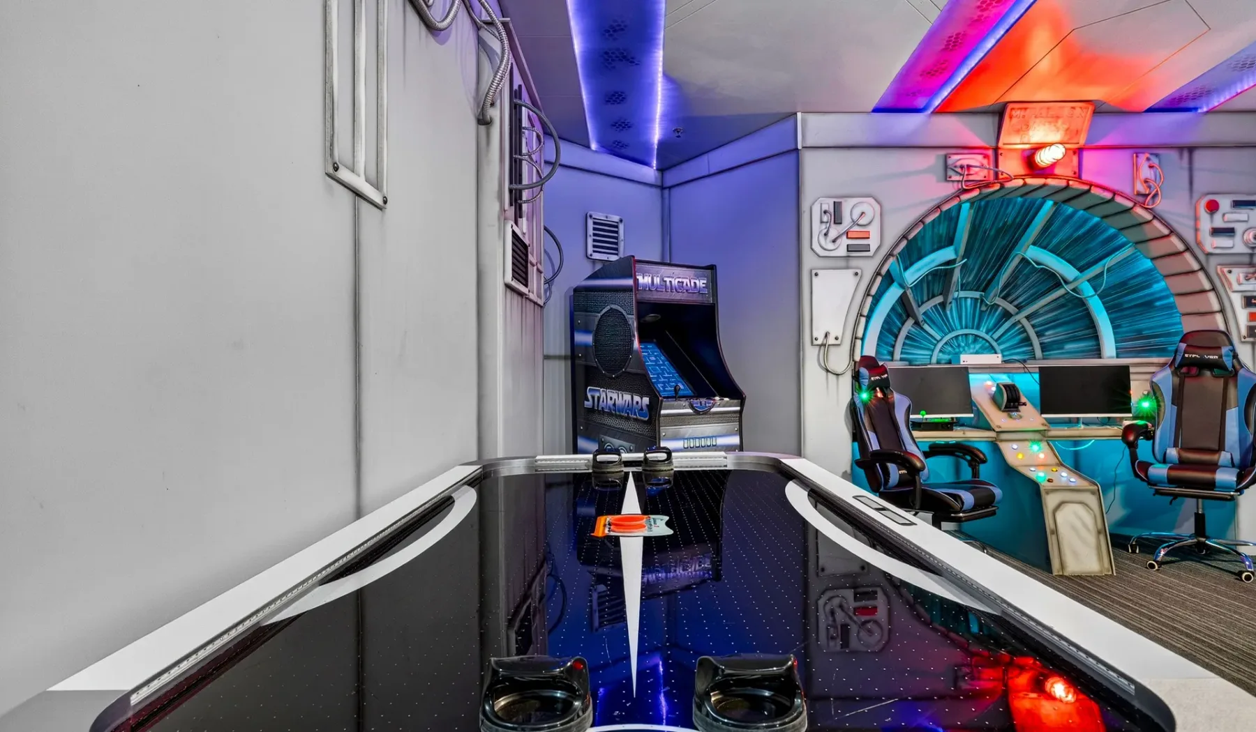 A colorful arcade room features a glossy air hockey table and arcade machines.