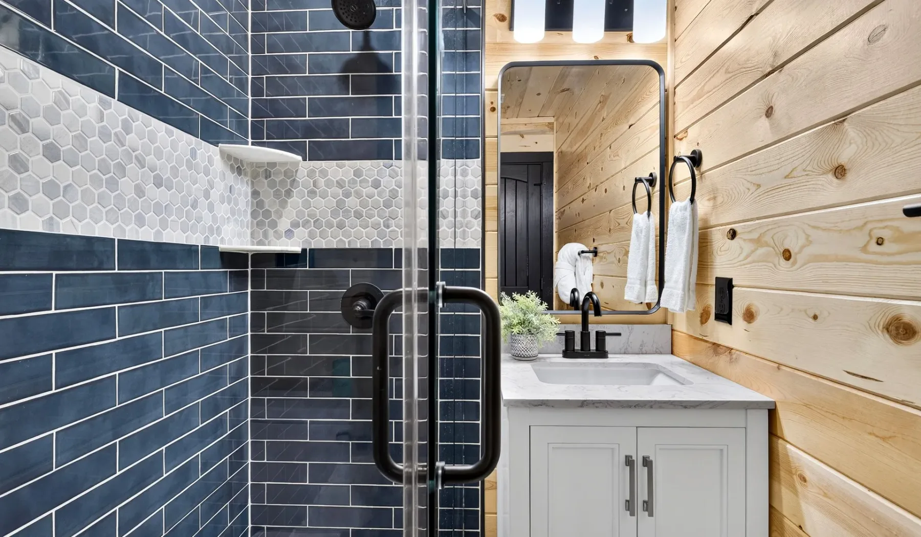 A bathroom with a dark tiled shower beside a light wood vanity.