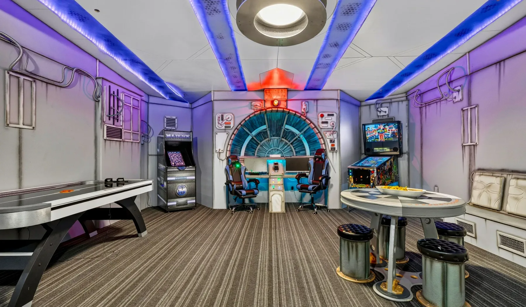 A futuristic game room with arcade machines and a central control console.