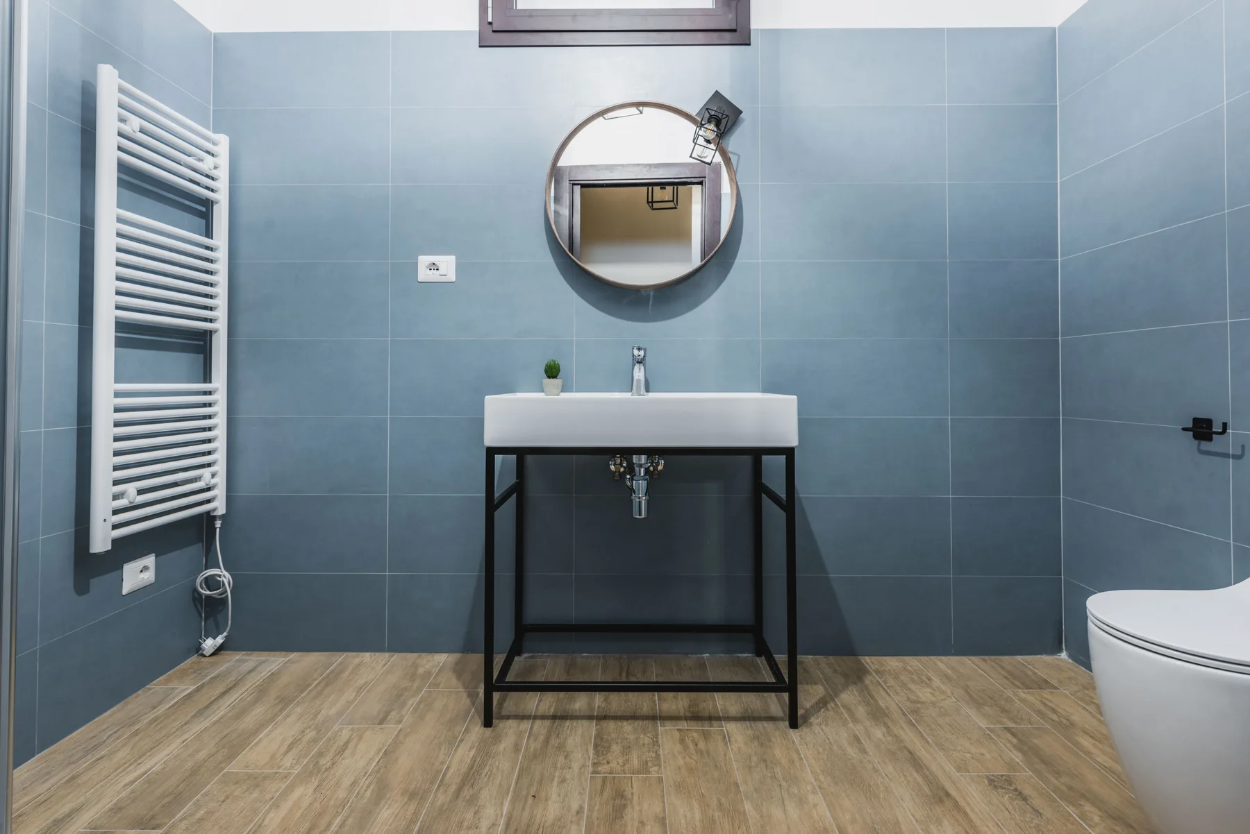 Un baño con paredes alicatadas, lavabo suspendido, espejo redondo y toallero calefactable.