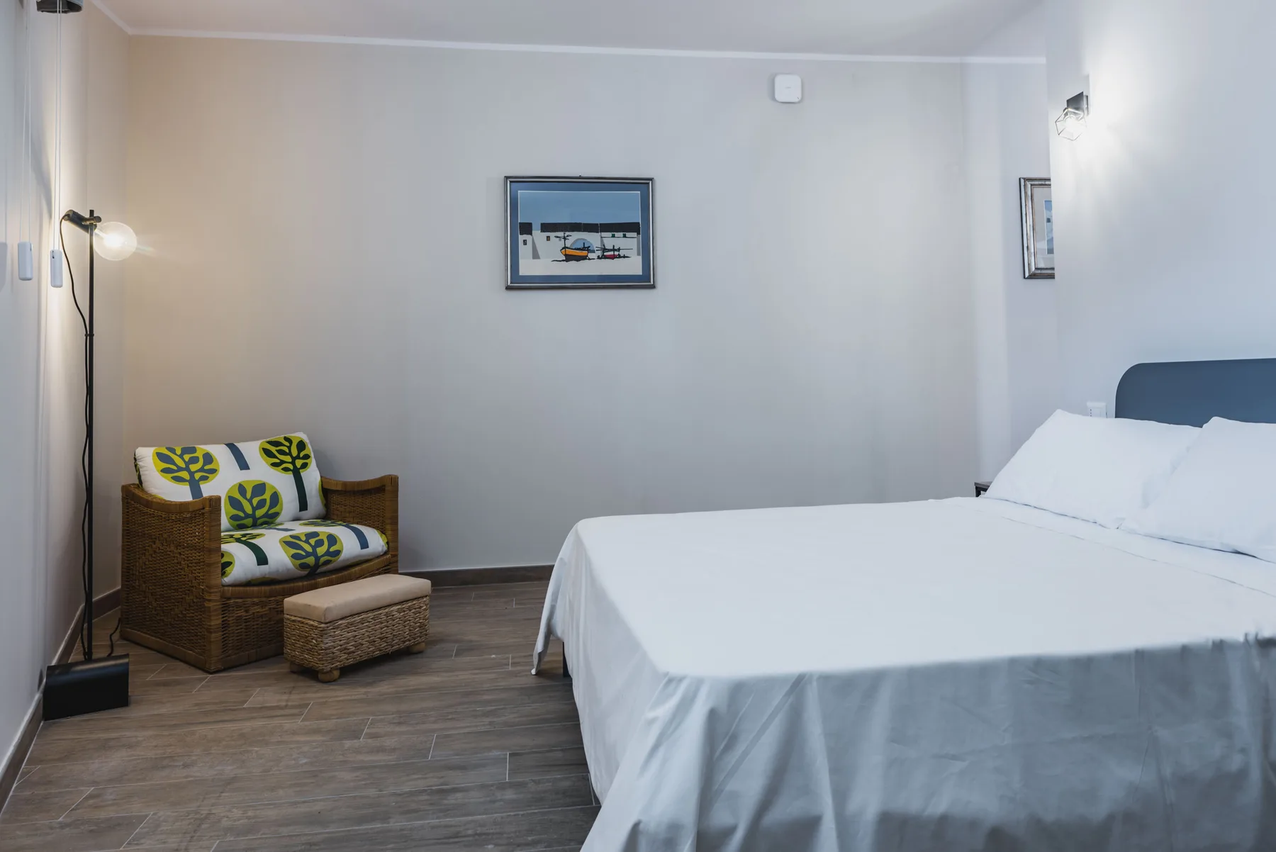 Un dormitorio con una cama bien tendida y un sillón de mimbre al lado.