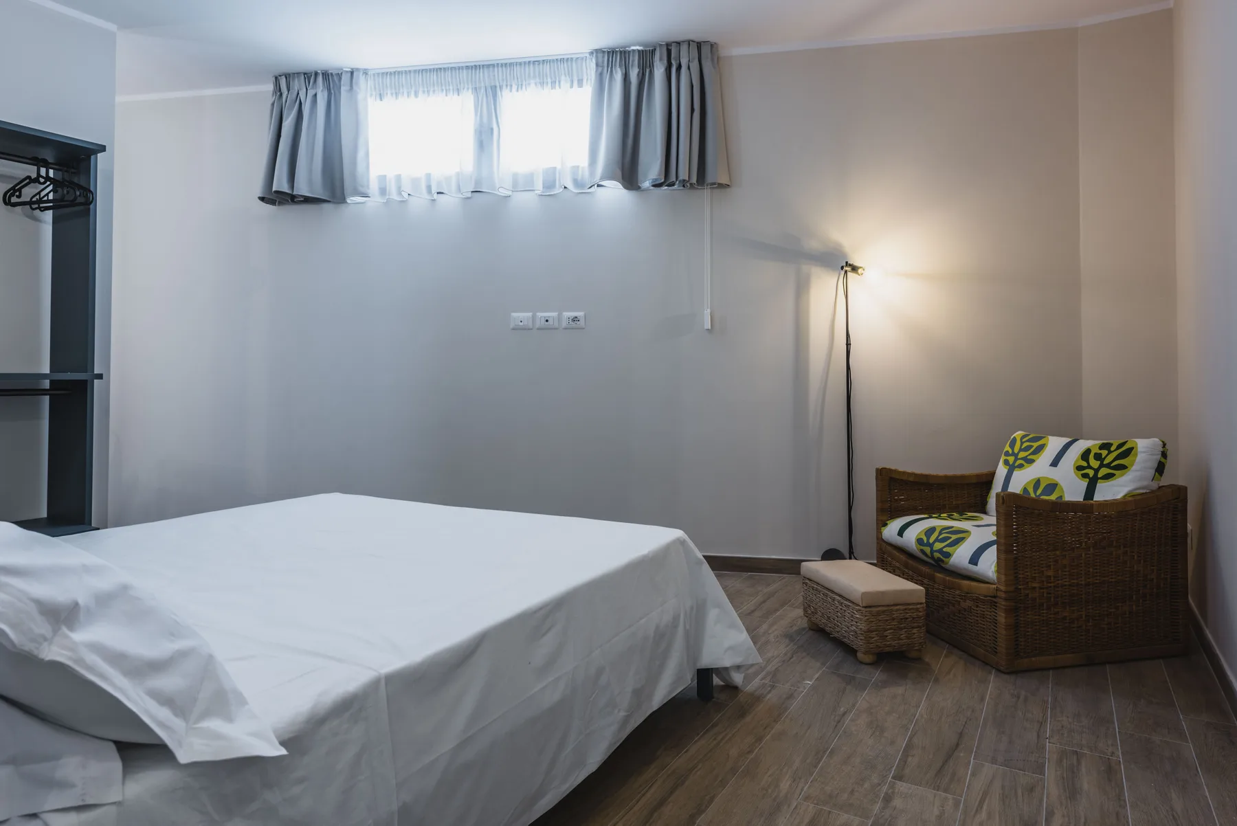 Un dormitorio con una cama y una zona de asientos de mimbre junto a una lámpara de pie.
