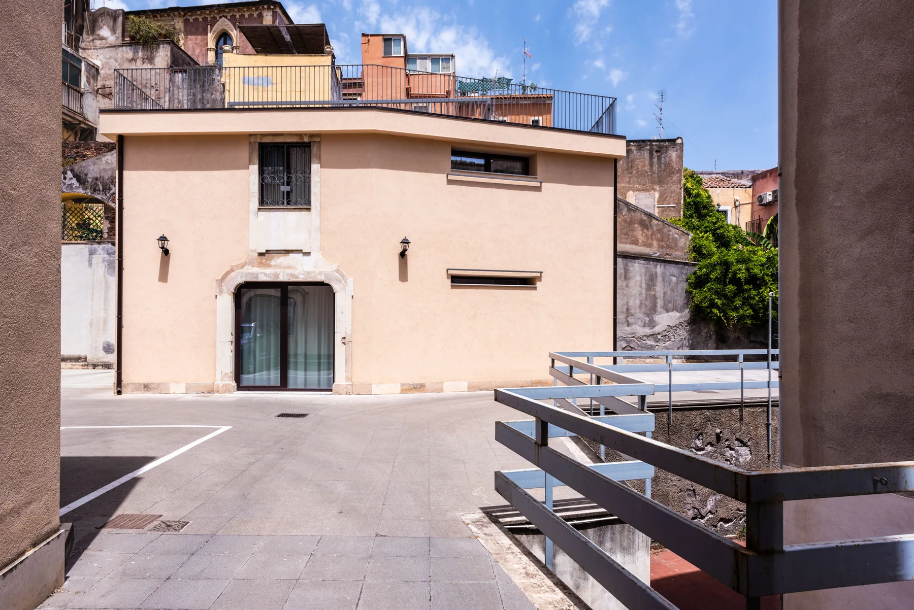 Una terraza exterior pavimentada junto a un edificio claro con una barandilla metálica.