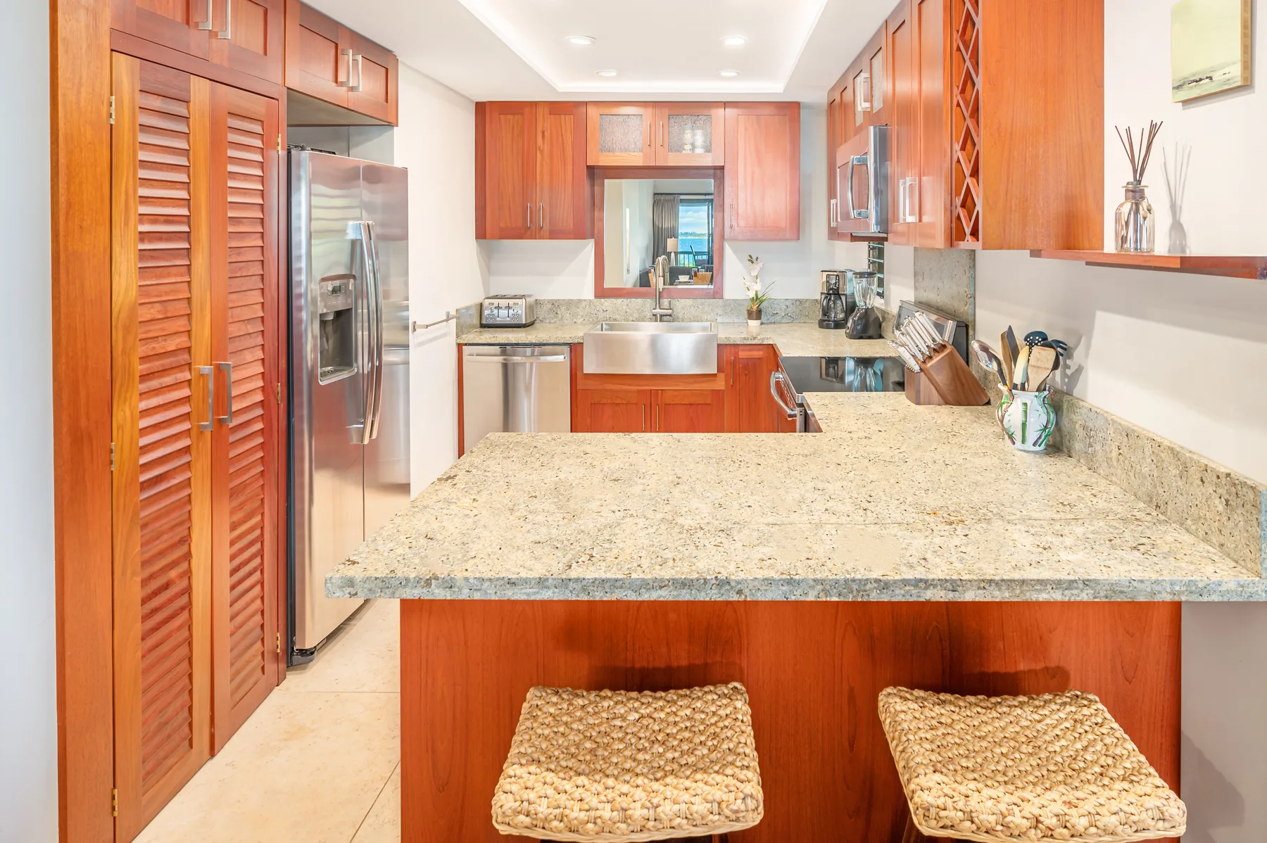A bright kitchen with wooden cabinets, a stone counter, and two woven stools.
