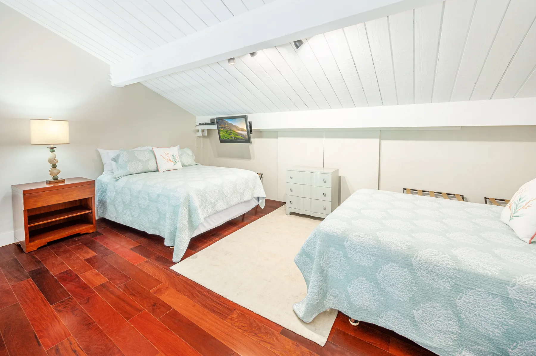 A bedroom with two beds, pale bedding, and a light rug.