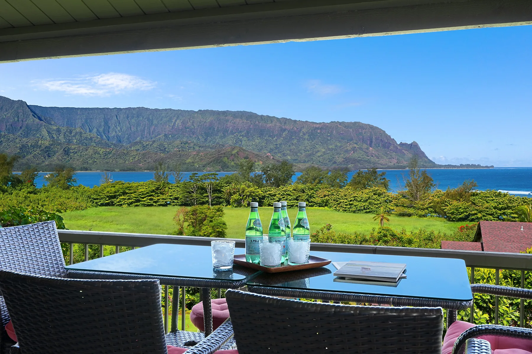 An outdoor patio table overlooks green grounds, blue water, and a mountain ridge.