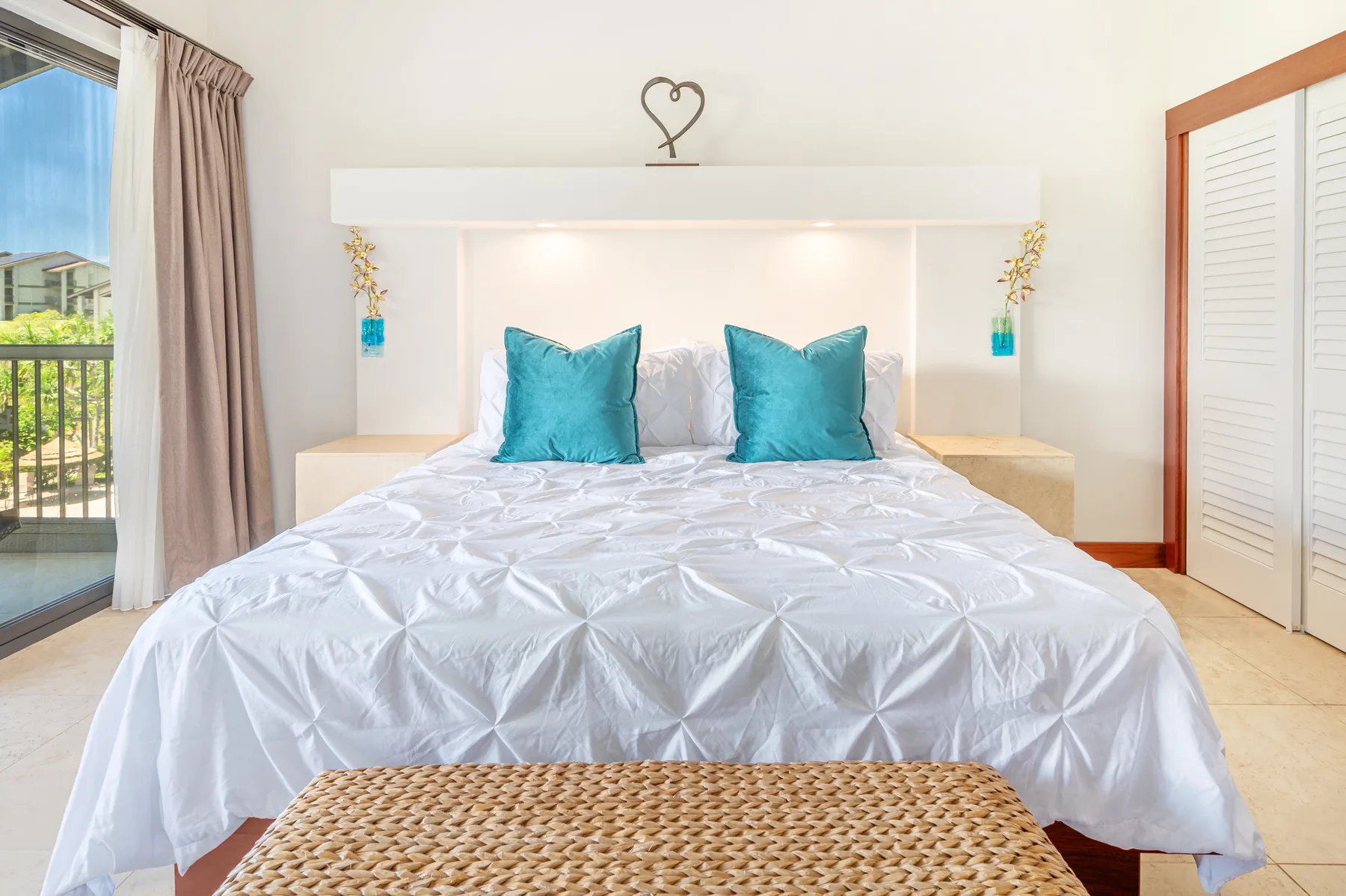 A bright bedroom with a neatly made bed and turquoise pillows.