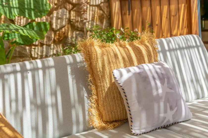 A cushioned outdoor seating area with decorative pillows in dappled sunlight.