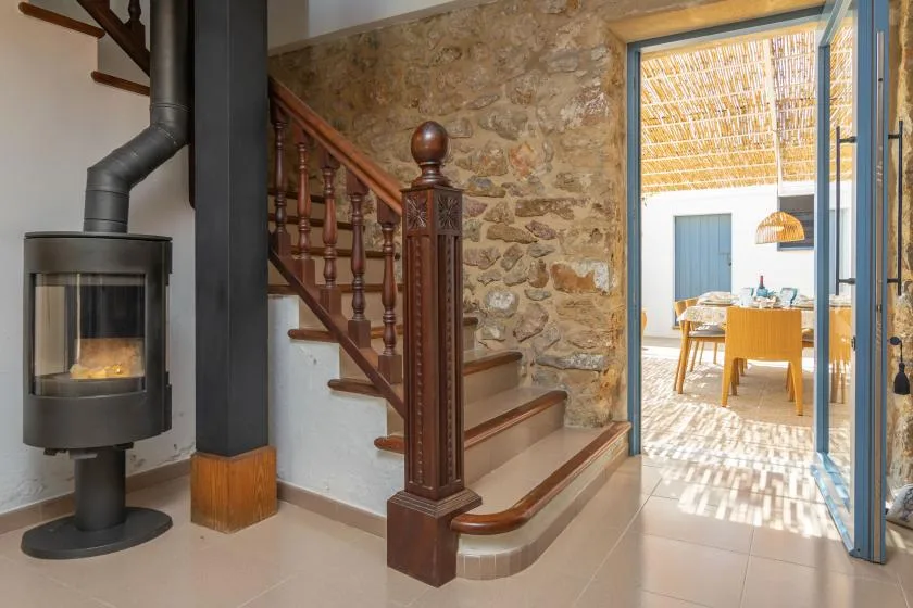 A stone-walled interior with a wooden staircase and a view into a dining area.
