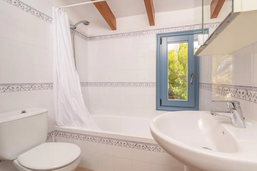 A tiled bathroom with a bathtub, shower curtain, sink, and window.