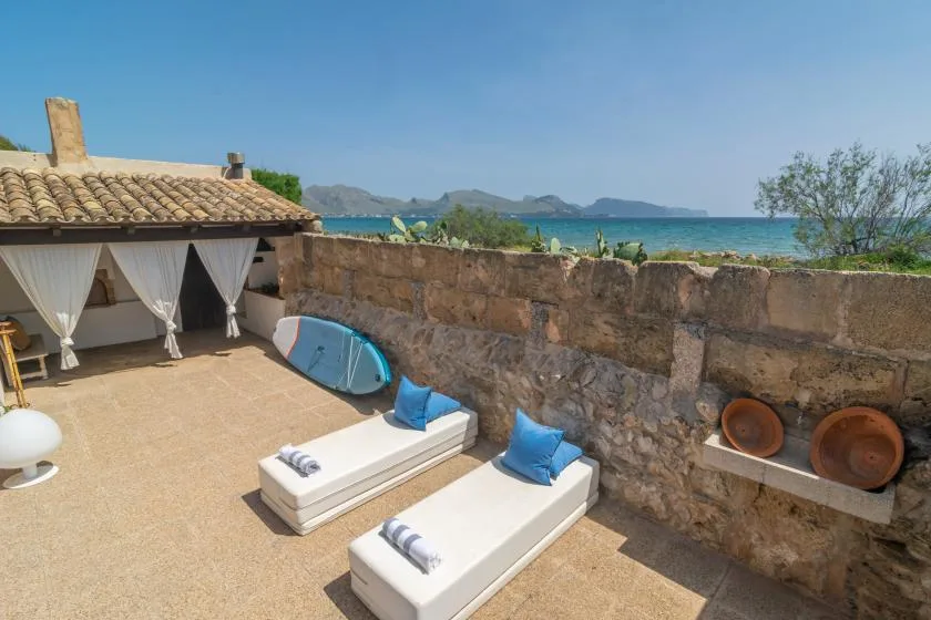 An outdoor patio with cushioned loungers and a stone wall overlooking the sea.