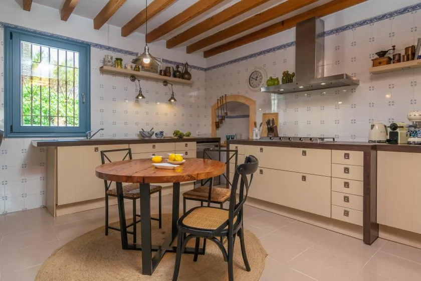 A tiled kitchen with a wooden dining table and chairs beneath exposed ceiling beams.