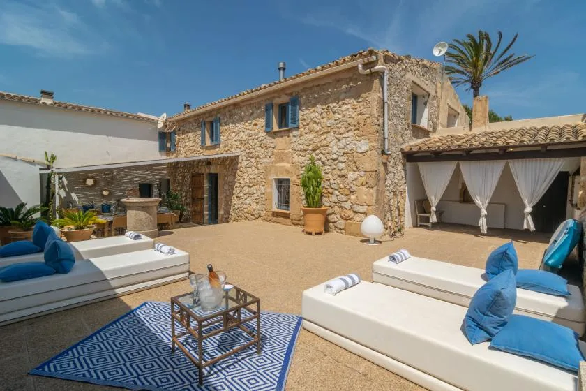 A sunny courtyard with lounge seating, a stone building, and a covered outdoor dining area.