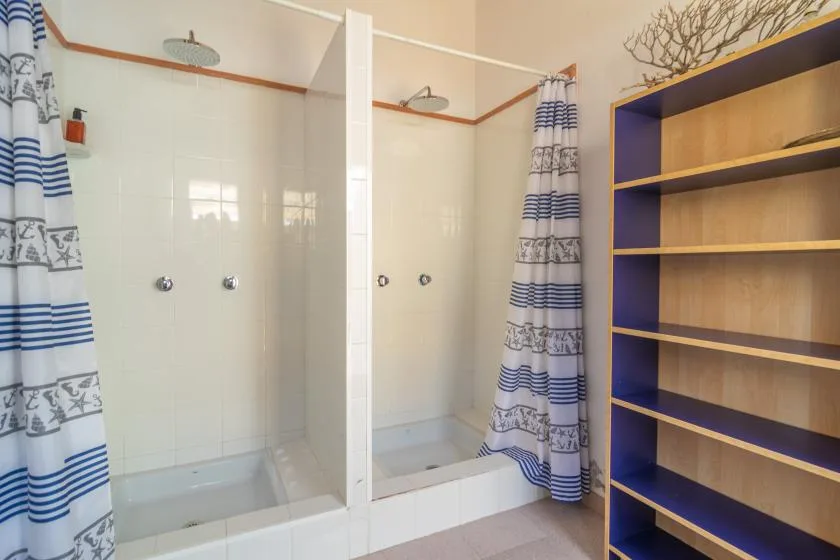 A tiled bathroom with shower curtains and open shelving.