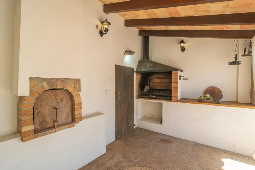 A rustic indoor cooking area with a brick fireplace and built-in grill.
