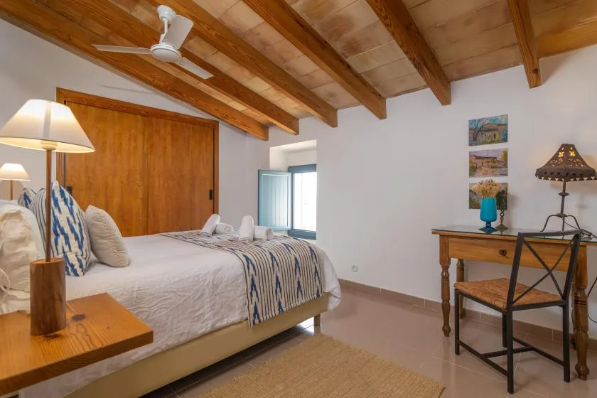 A bedroom with a bed beneath exposed wooden ceiling beams.