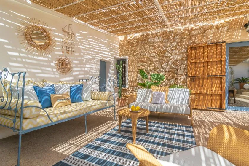 A sunlit outdoor lounge with cushioned seating and a woven shade roof.